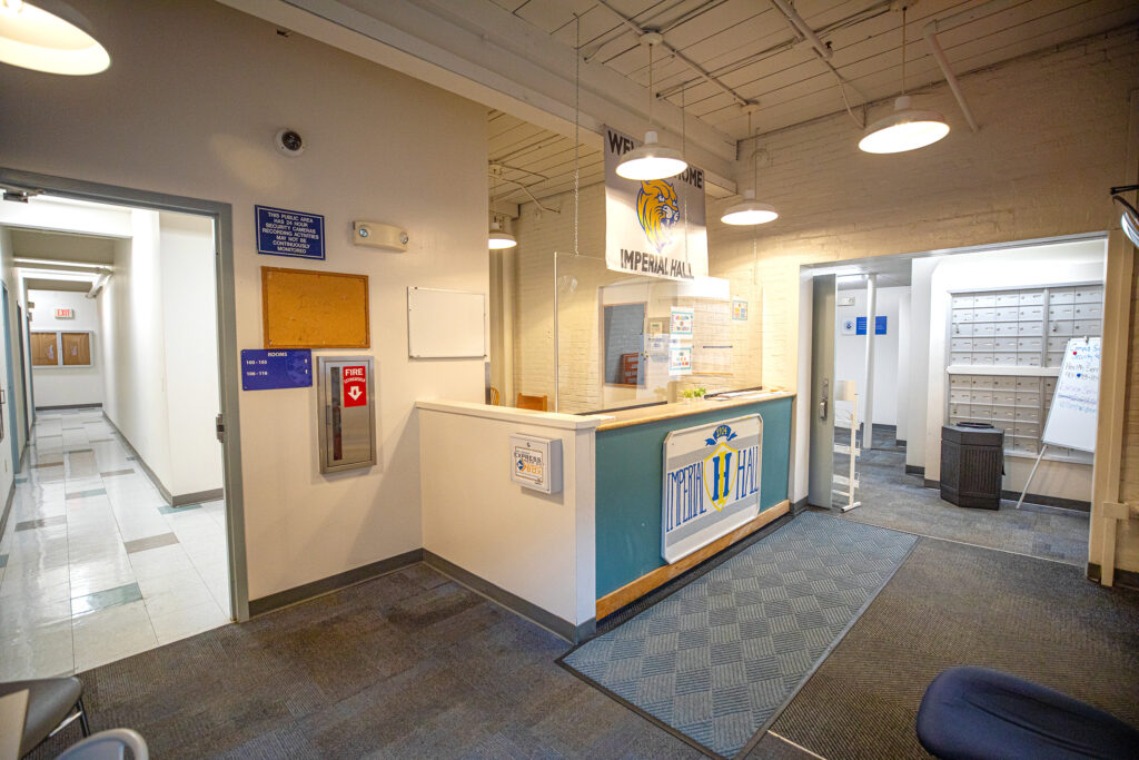 The reception area of Imperial Hall features a front desk with a logo, a hallway leading to rooms, and a mailroom with lockers.