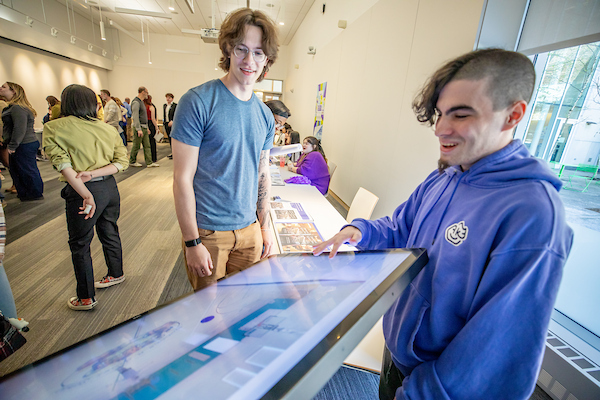Two individuals interact with a large touchscreen display in a brightly lit, bustling indoor space.