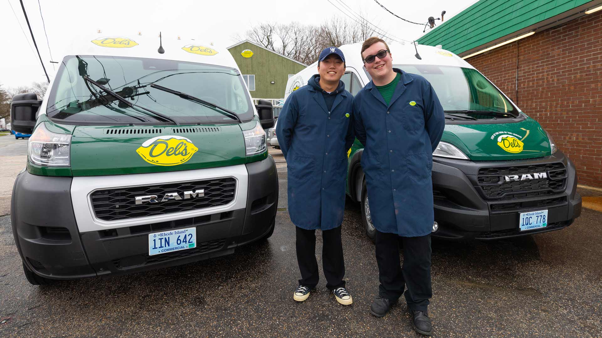 photo of Sang Hoon Chae u201923 and Caleb Atkinson u201924 posing in front of two Delu2019s delivery trucks in a parking lot