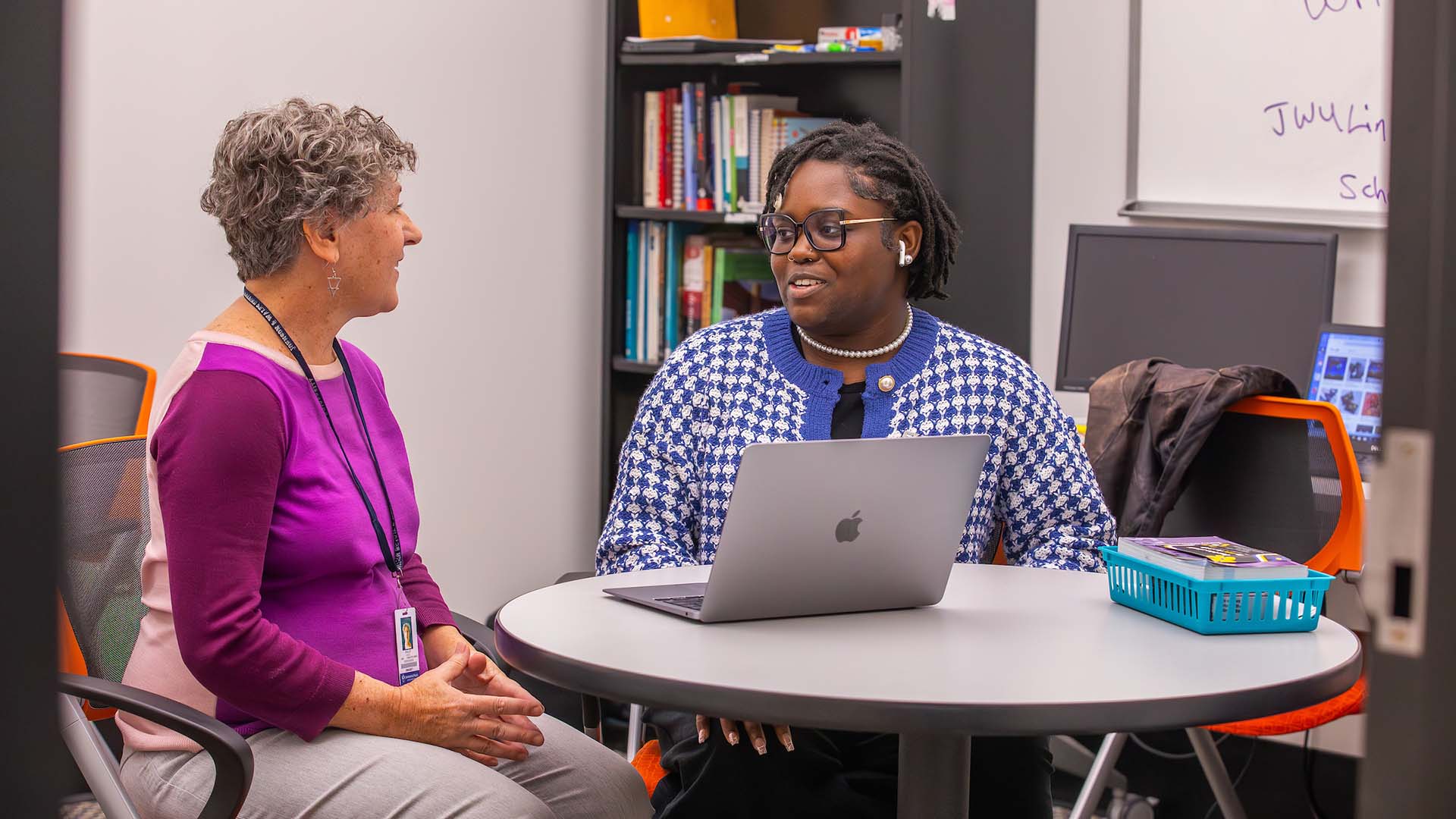 Two women sitting at a table with a laptop in front of them.