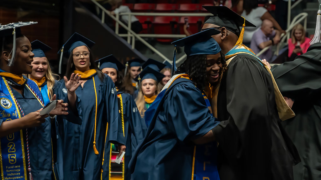 Two new grads share a tearful hug while their friends cheer them on.
