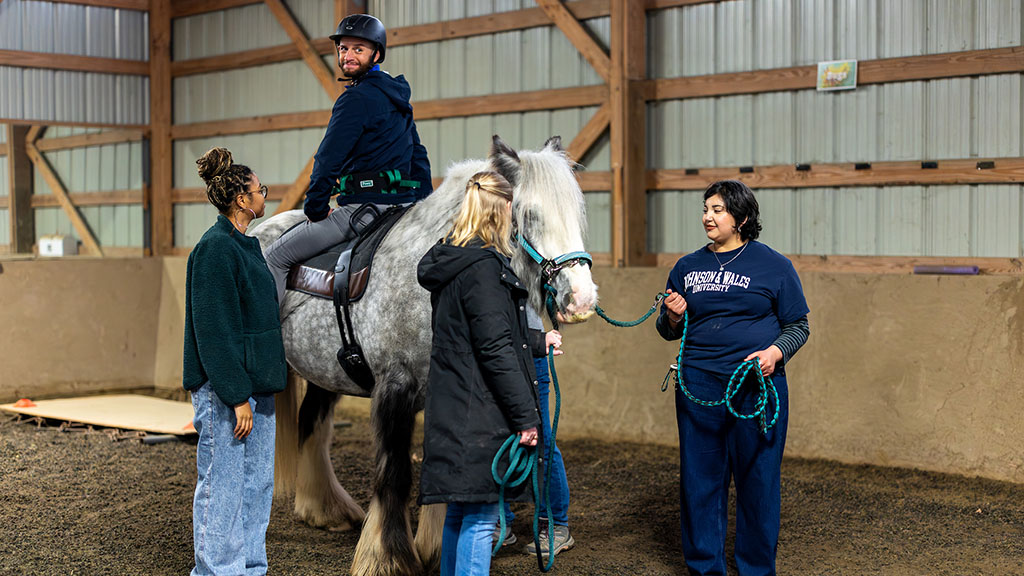 A man sitting backwards on a horse with students observing