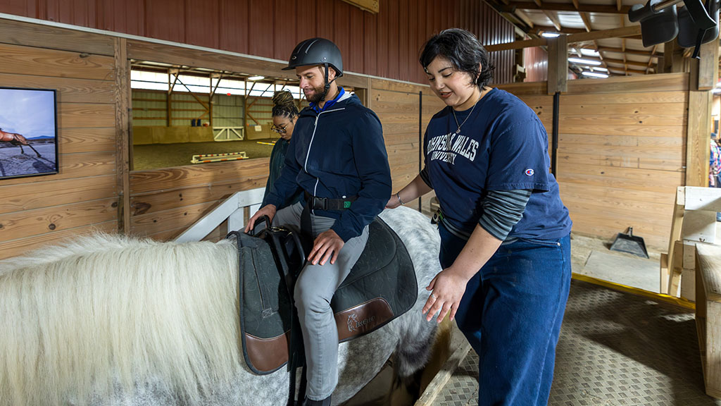 A woman standing next to a man sitting on a horse