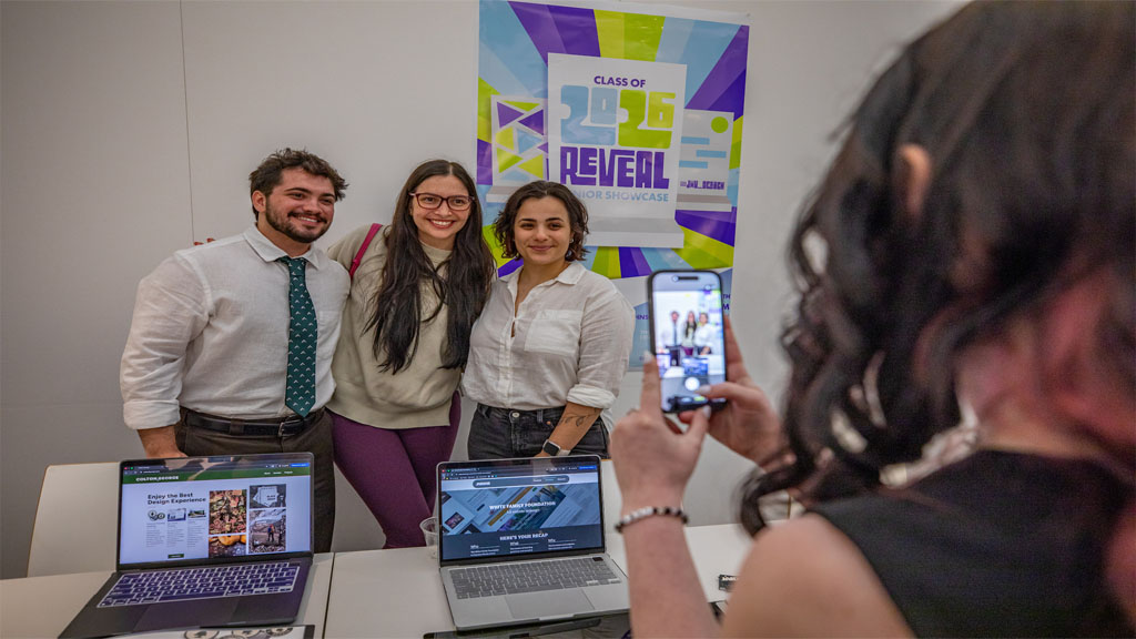 Design students posing for photo in front of REVEAL poster
