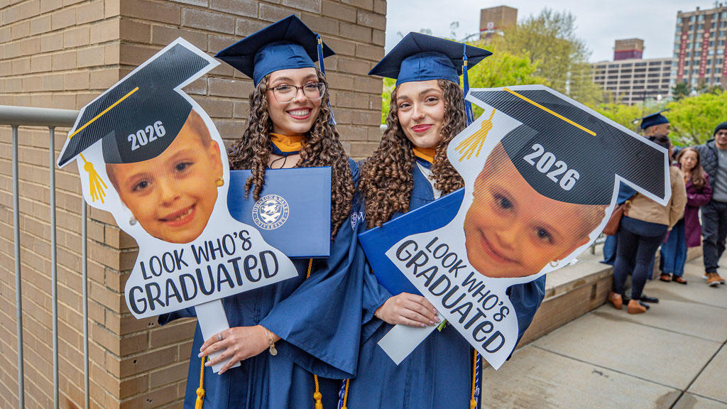 Twin graduates hold up signs reading, “Look Who’s Graduated?”