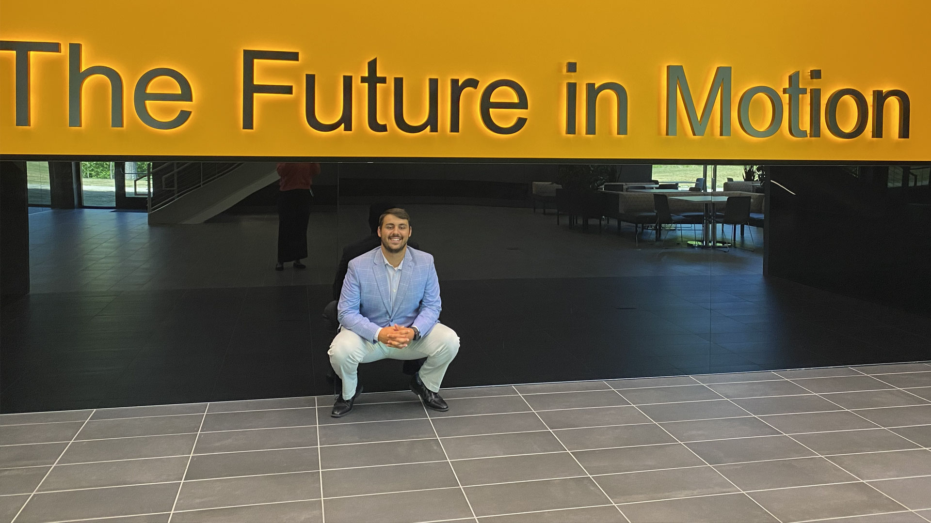 John Billinis u201926 in front of a sign reading, u201cThe future in motion.u201d